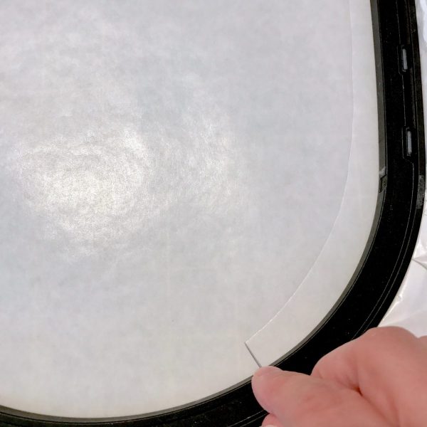 Hoop a piece of Sticky Tearaway Stabilizer in the appropriate size hoop for your project, waxy paper side up. Use a pin to score the wax paper topping, all the way around the inner edge of the hoop.