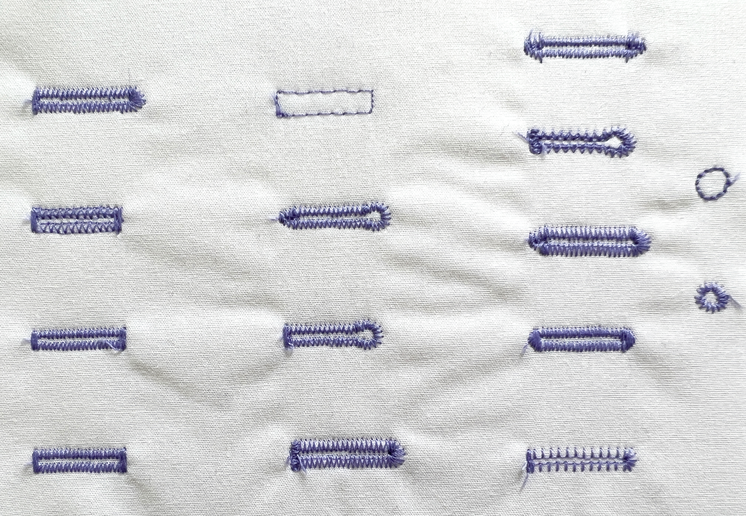 A grid of 13 buttonholes and 2 eyelets sewn with purple thread on white fabric.