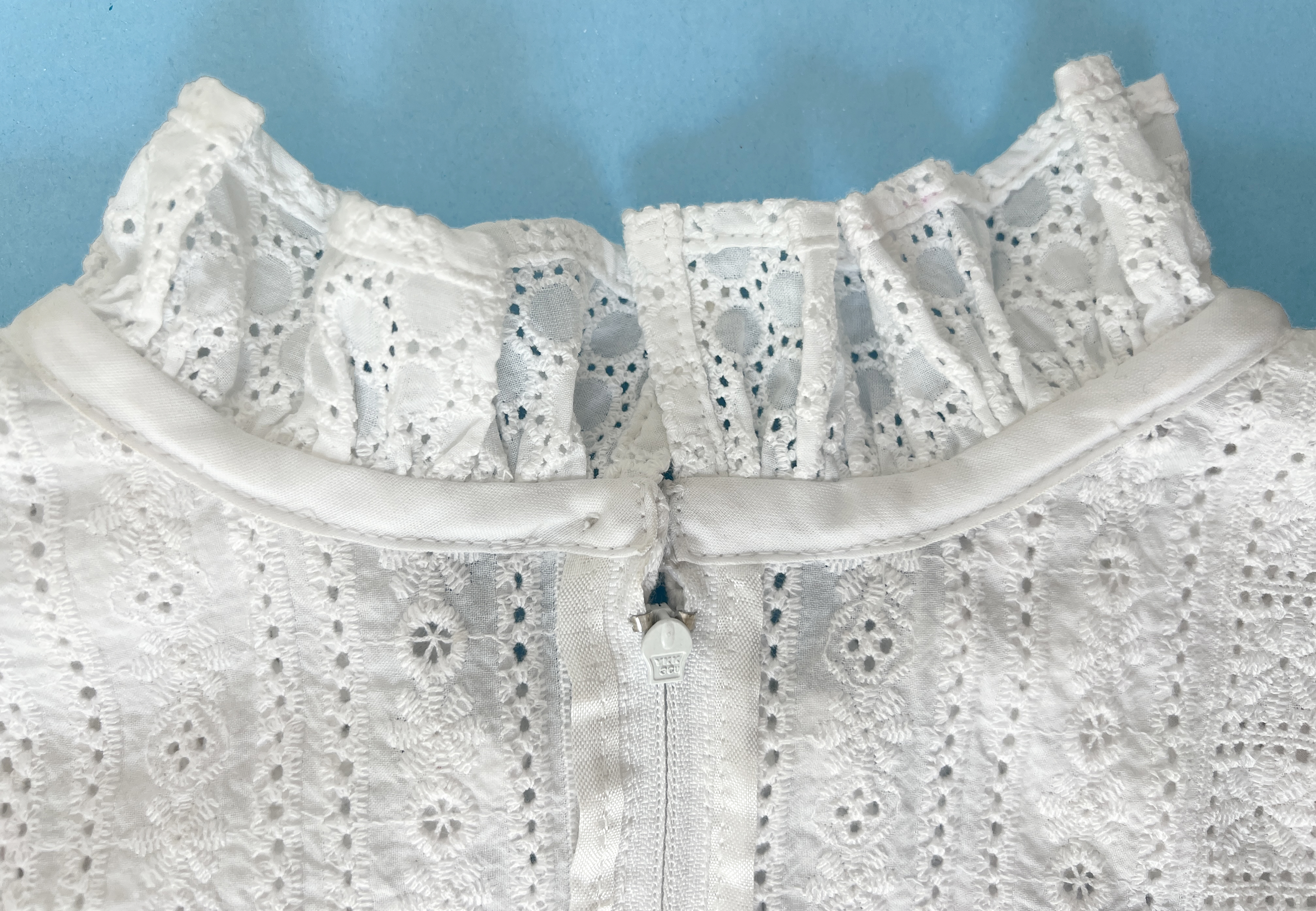 Details of the inside of a white eyelet dress. The neckline has a ruffle and is finished with bias tape, the zipper tape is bound with rayon ribbon.