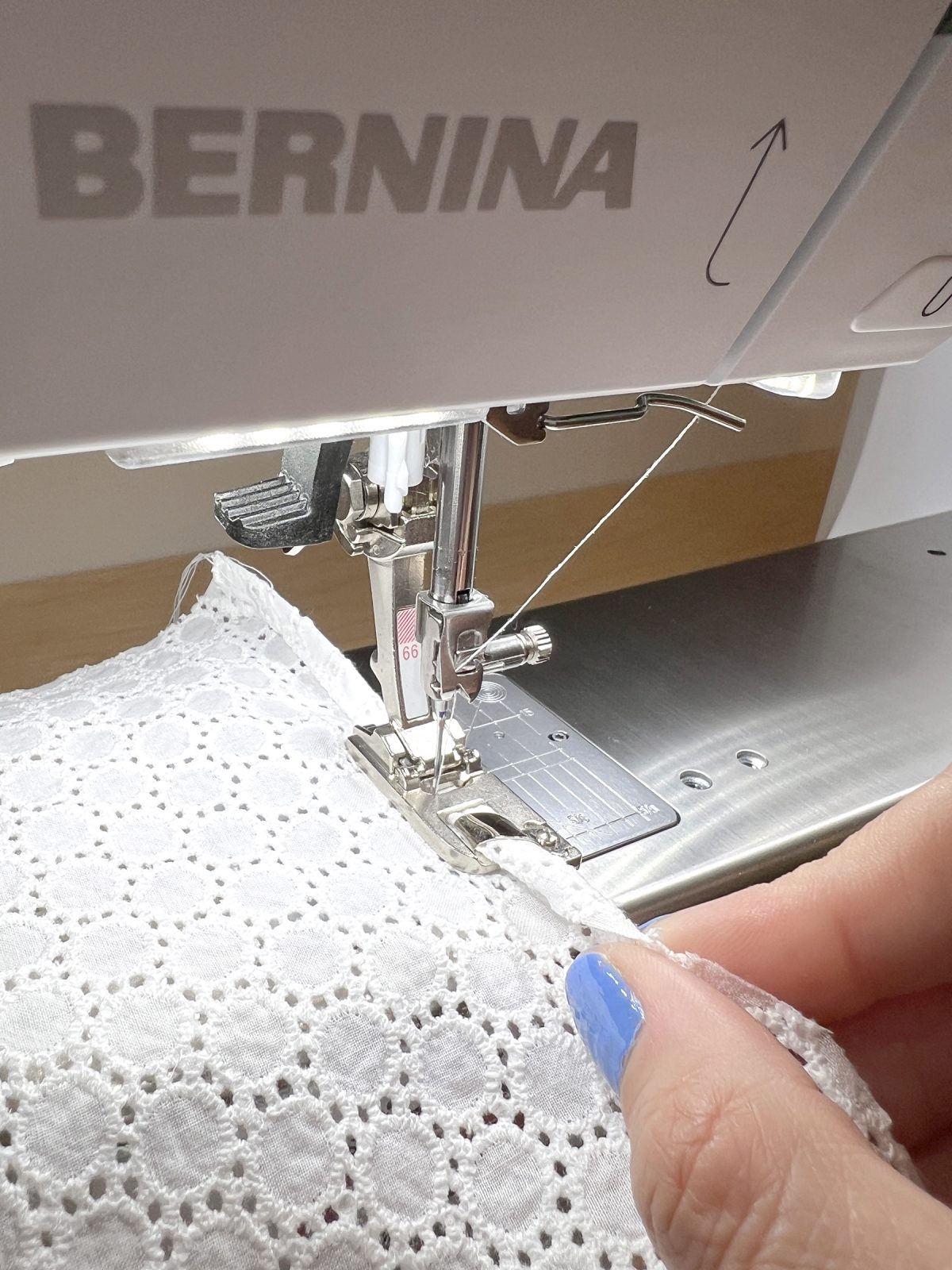 A hand pinches white fabric into a curved shape and feeds it into a sewing machine's rolled hemmer foot.