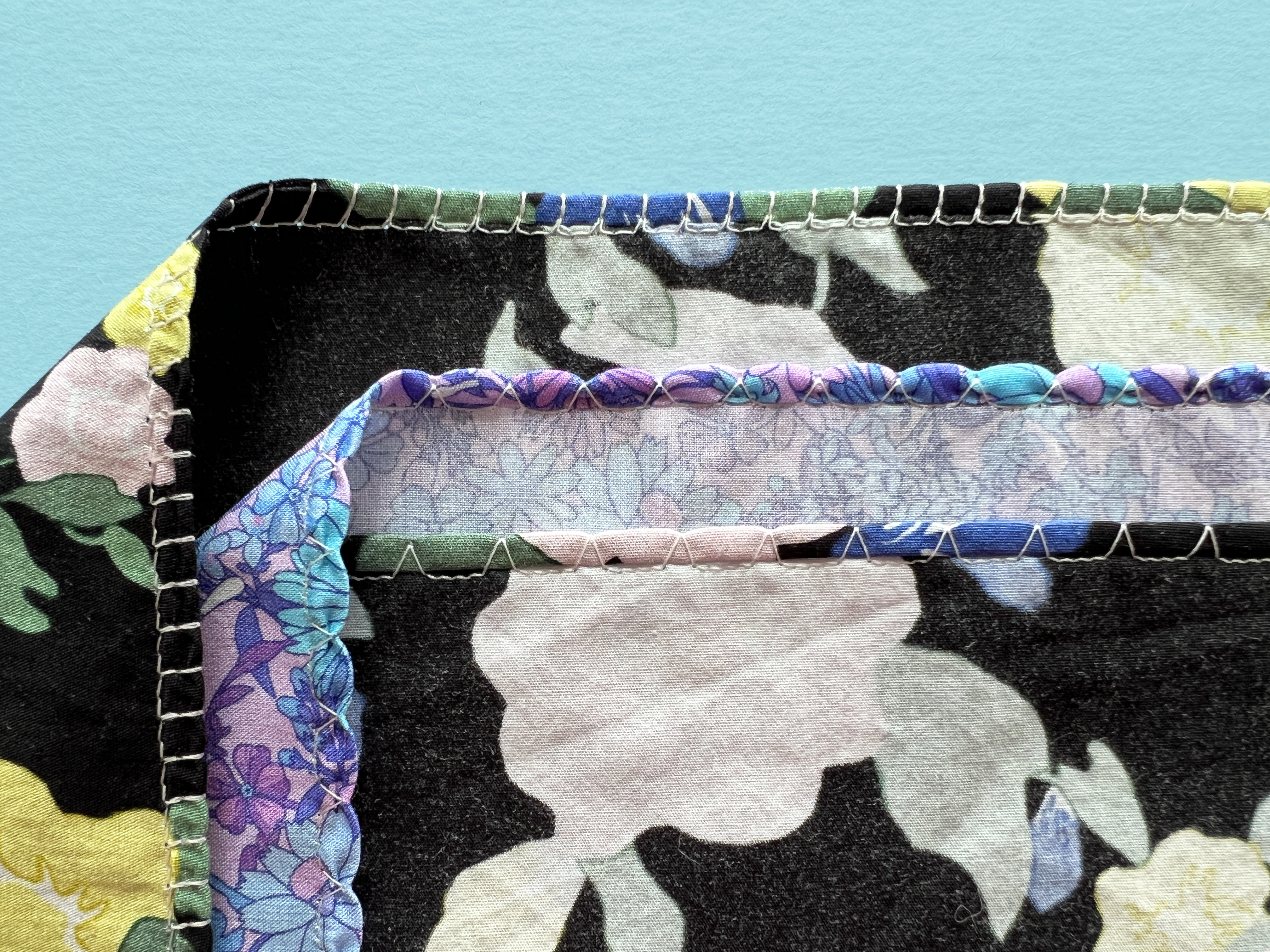 3 fabric swatches with rolled shell hems, each one achieved with a different sewing machine stitch.