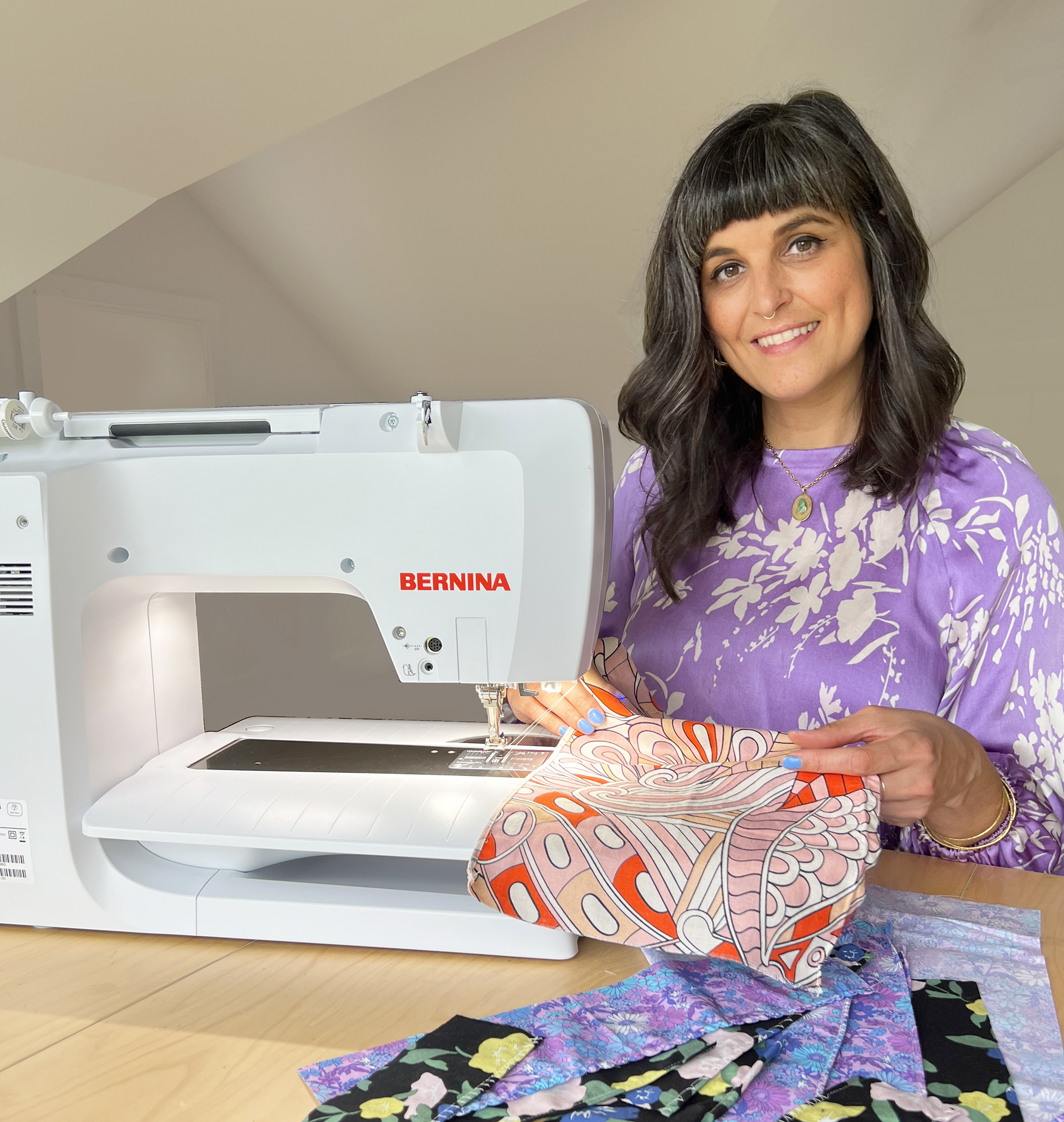 Martha is sitting at a BERNINA sewing machine. She is hemming an orange printed fabric, with an assortment of swatches in front of her.