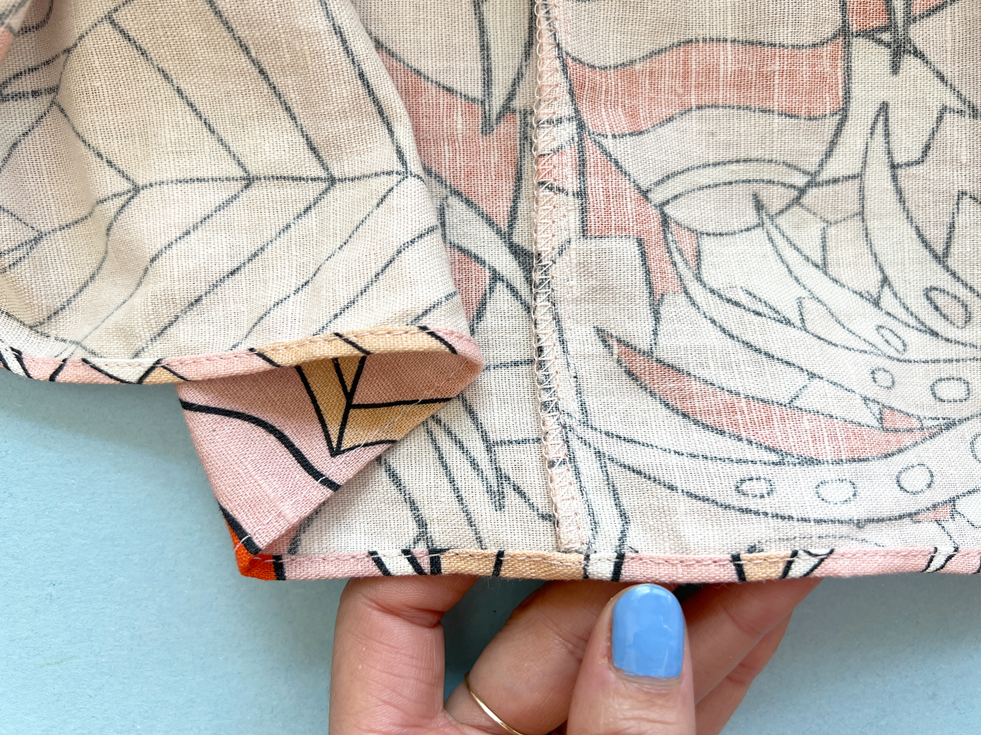 Close up image of a rolled hem that intersects a seam, the seam allowance has been finished with an overlocker.