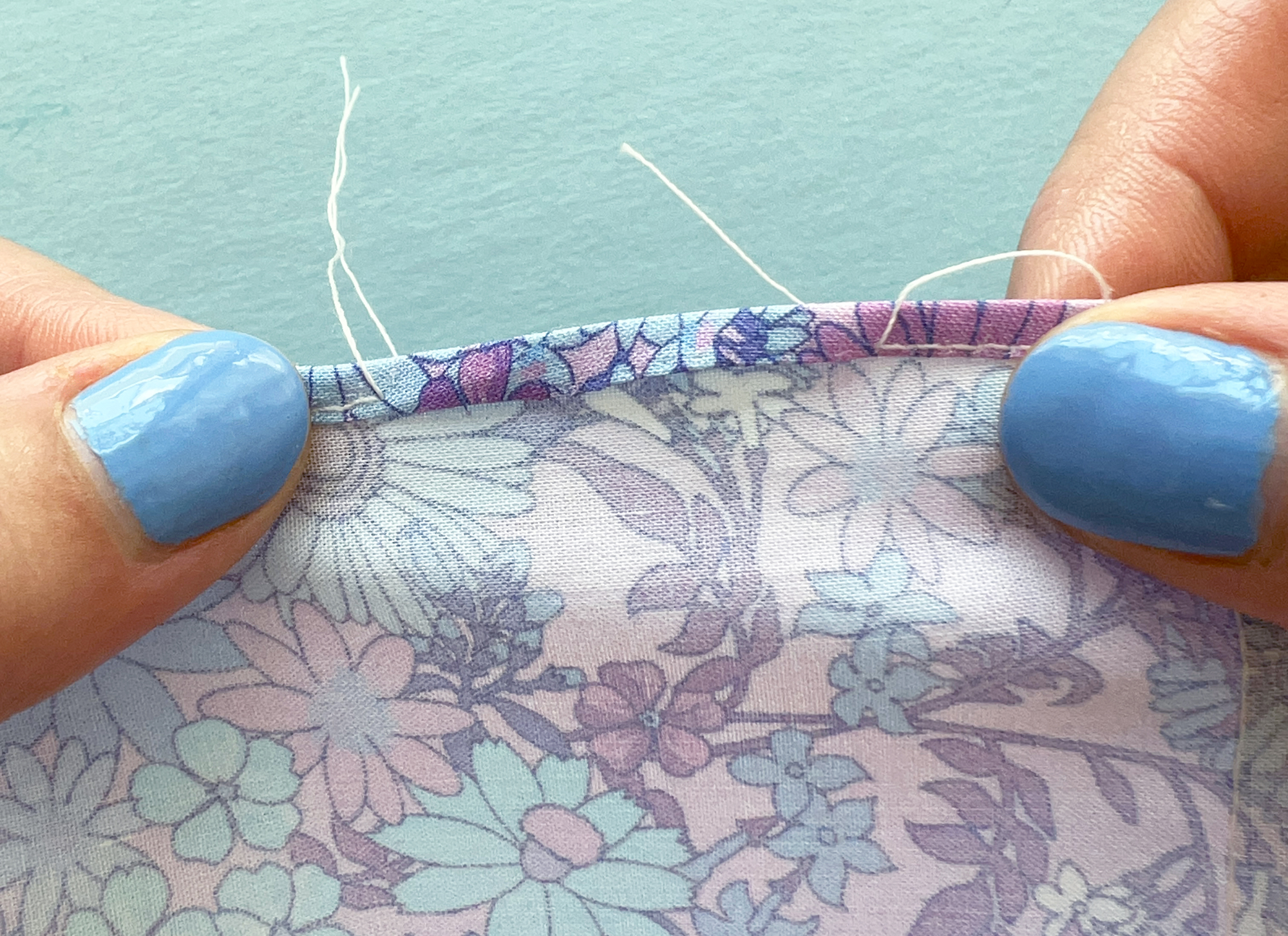 Close up shot of two thumbs pulling on a swatch of fabric to force the edge of the fabric to roll over and create a hem.