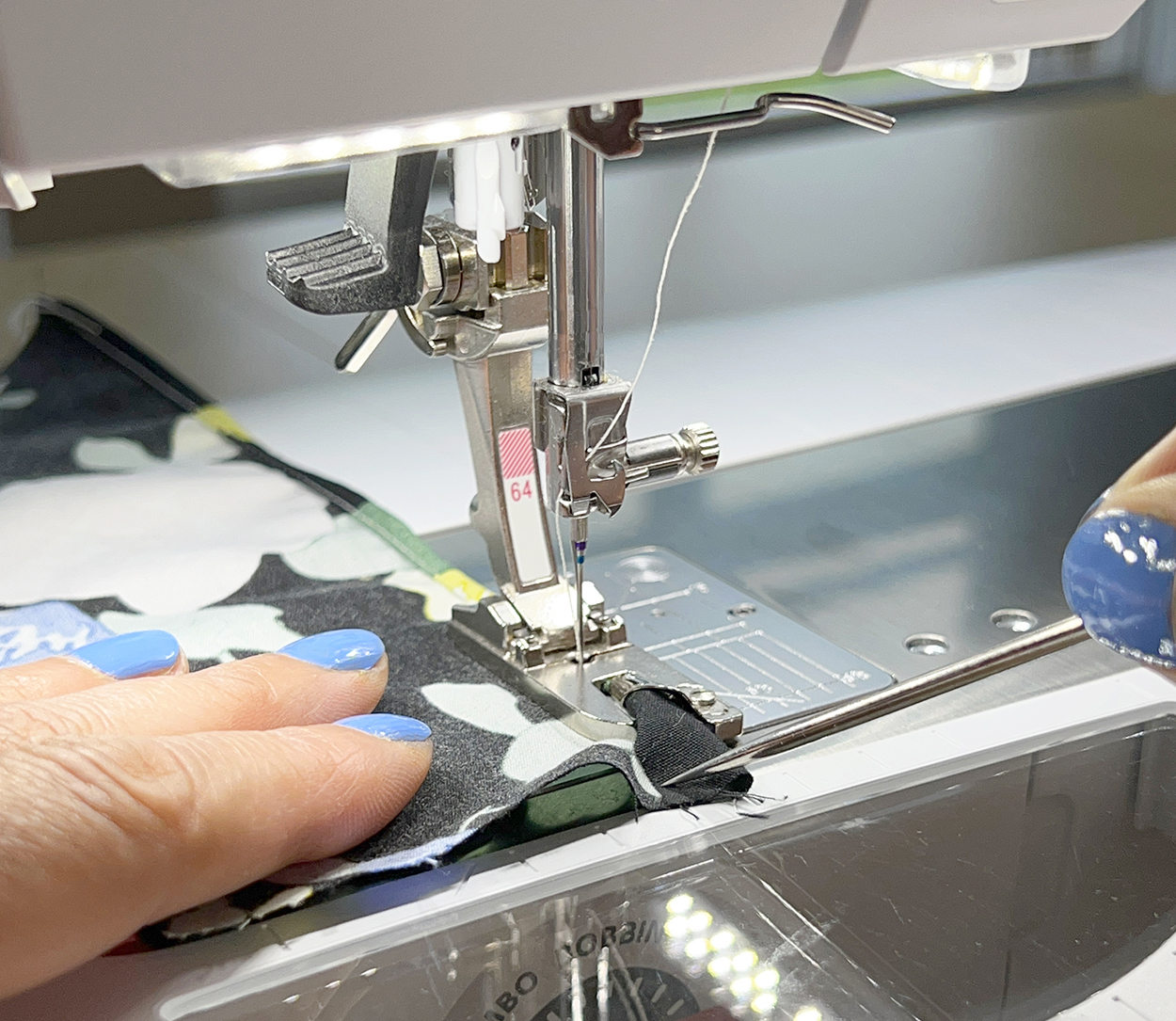 An awl is used to guide fabric into a sewing machine's hemmer foot.