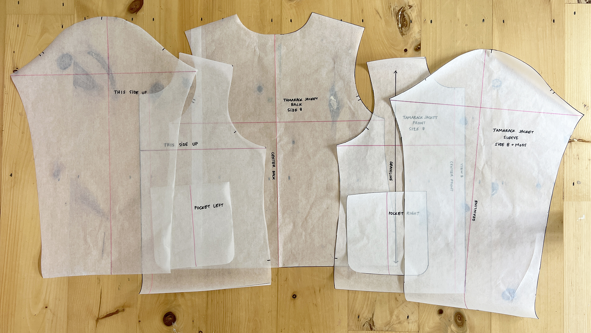 Pieces of white sewing pattern tissue, enough to make a jacket, are shown on a hardwood floor.