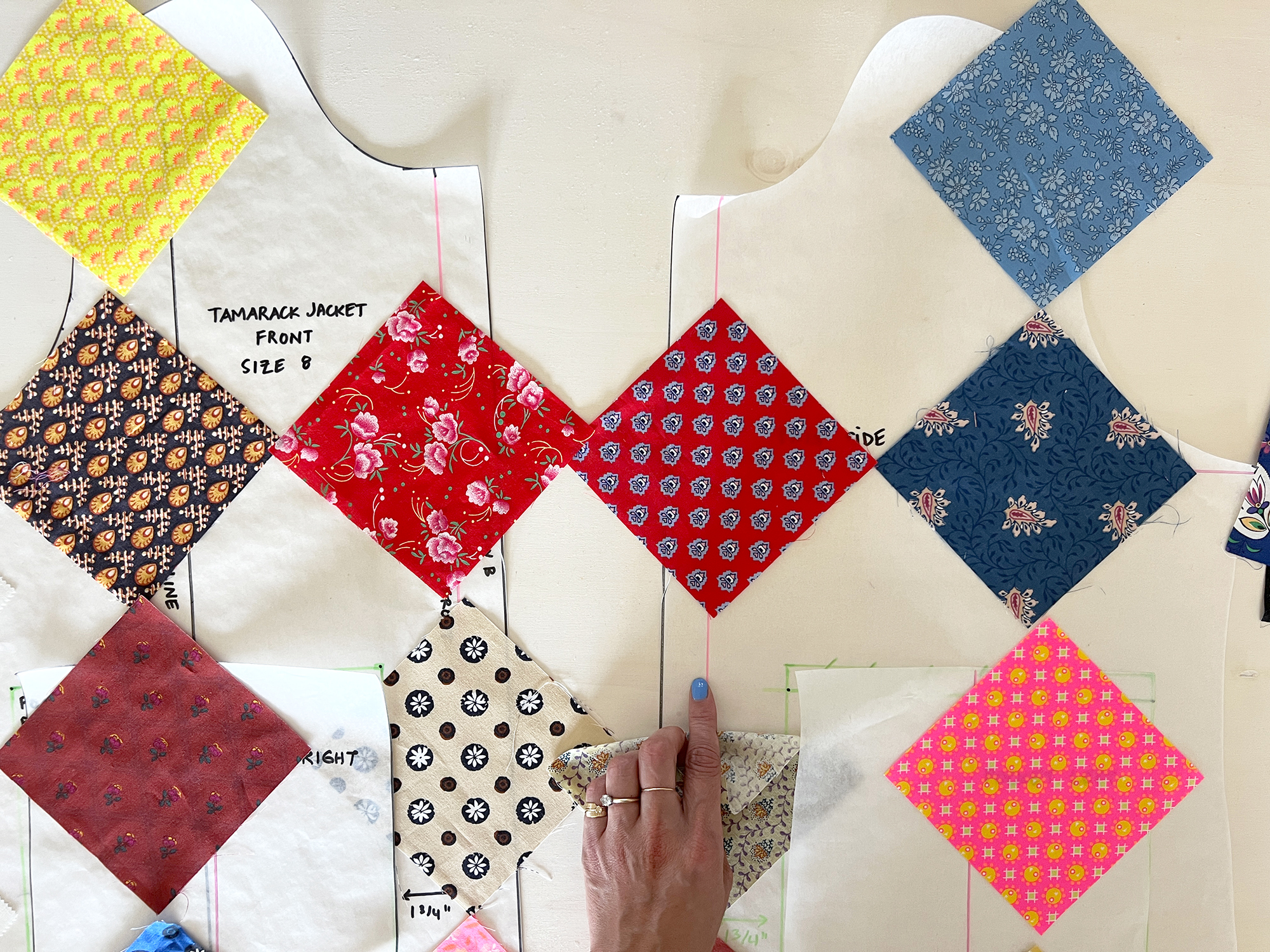 Different colored squares of fabric are laid out on top of a sewing pattern. A hand points to the Center Front line.