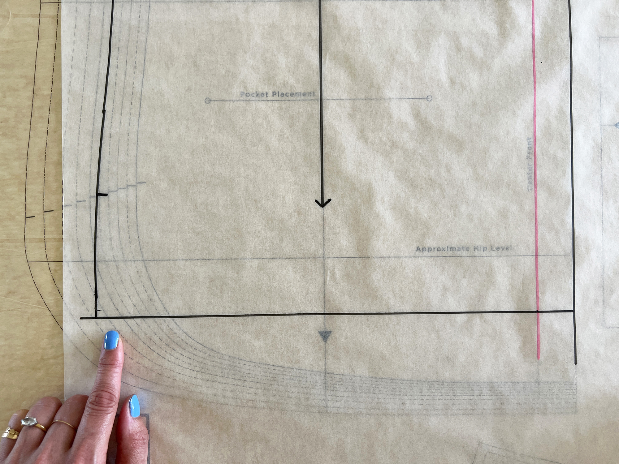 A hand is pointing to sewing pattern which has been modified to have a straight hem, instead of curved.