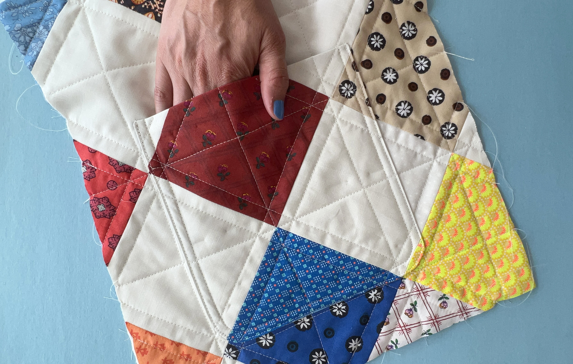 A hand slips inside a patch pocket on a quilted jacket, the patch pocket matches the patchwork design and blends in to the jacket.