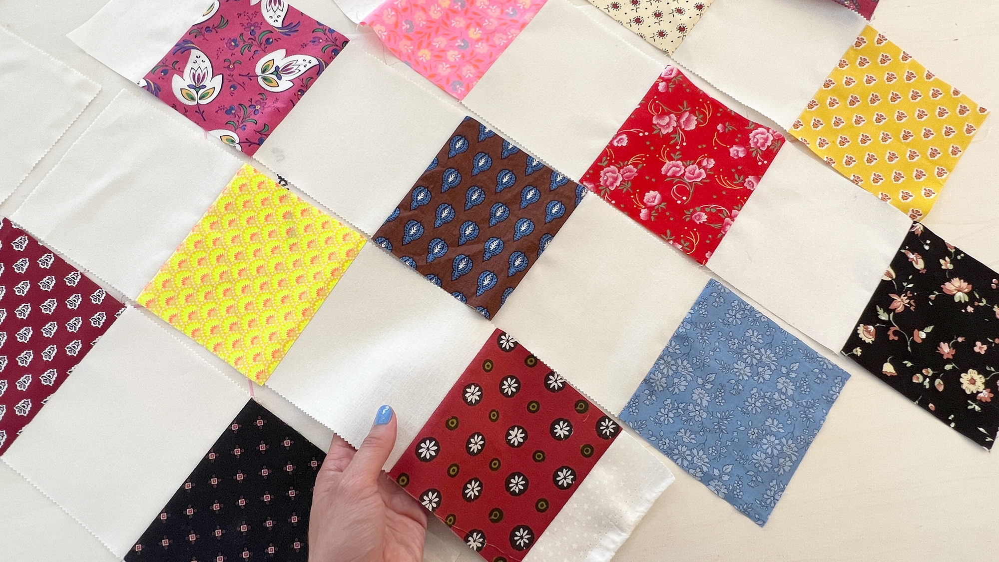 Checkerboard patchwork of multicolor fabrics and solid ivory colored fabric.