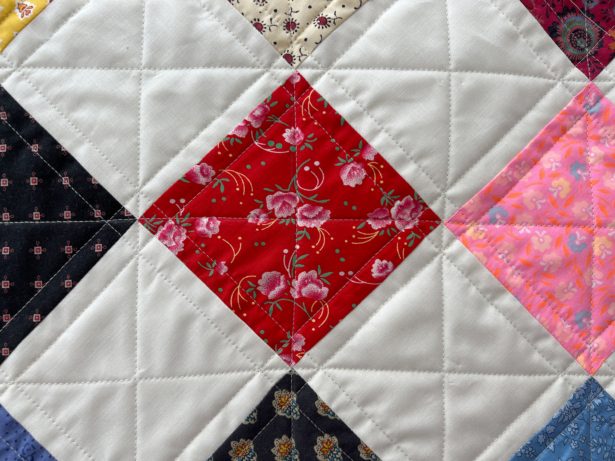 A close up photo of a quilt, it has colorful fabrics and white fabrics in a checkerboard arrangement.