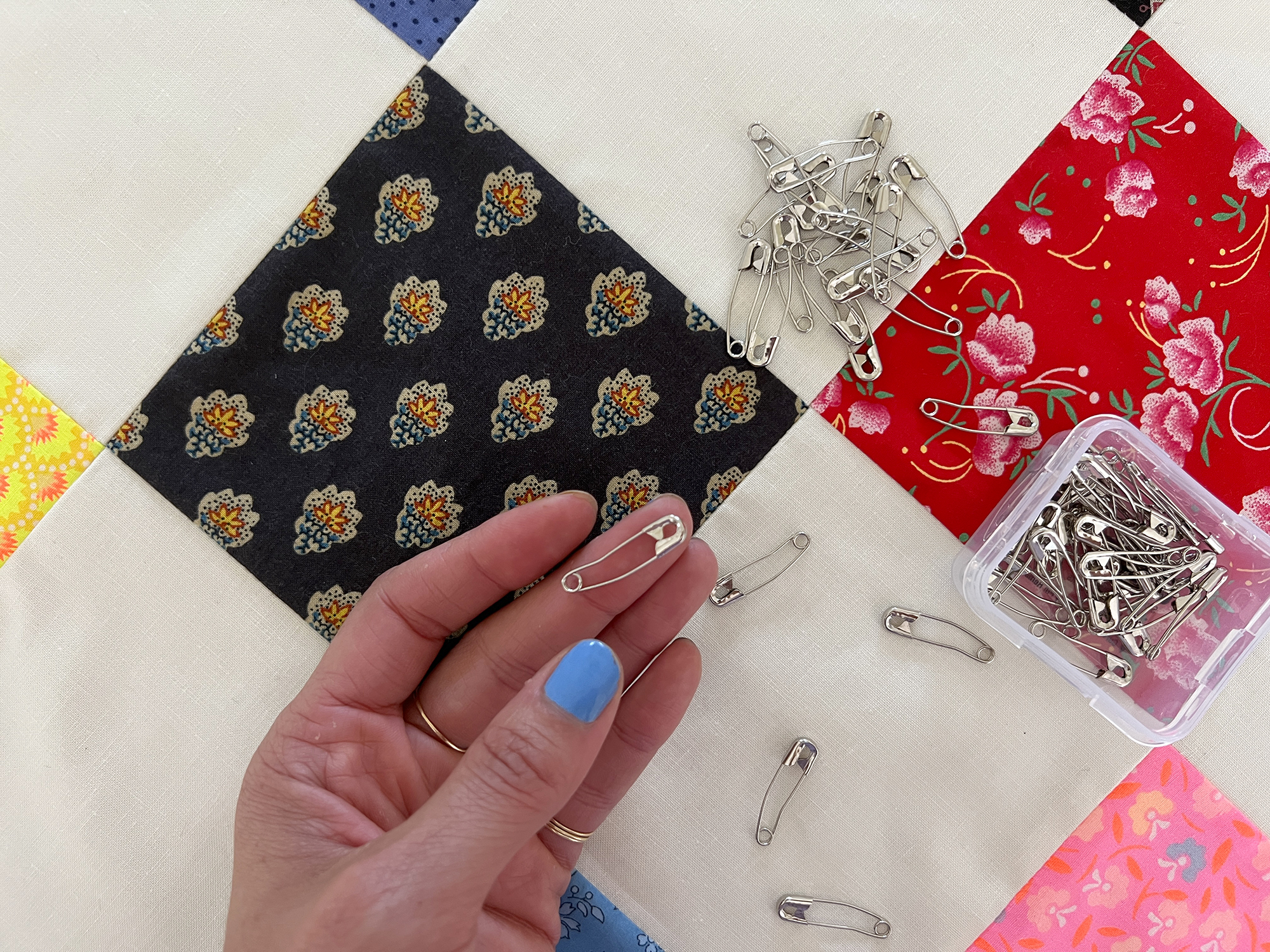 A hand holds a curved quilter's safety pin over a background of a quilt and more safety pins.