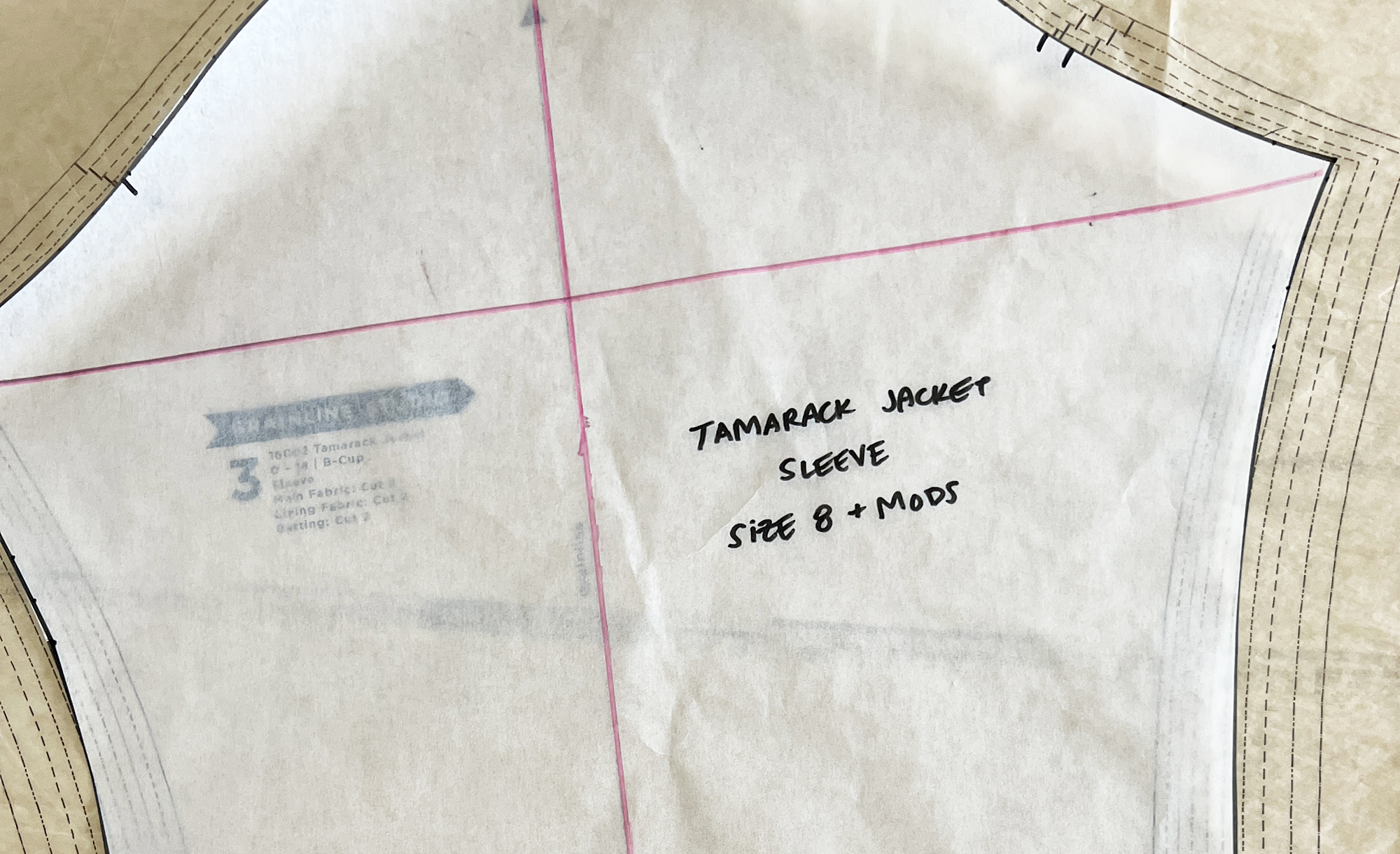 A sewing pattern for a sleeve has perpendicular lines drawn in pink marker.
