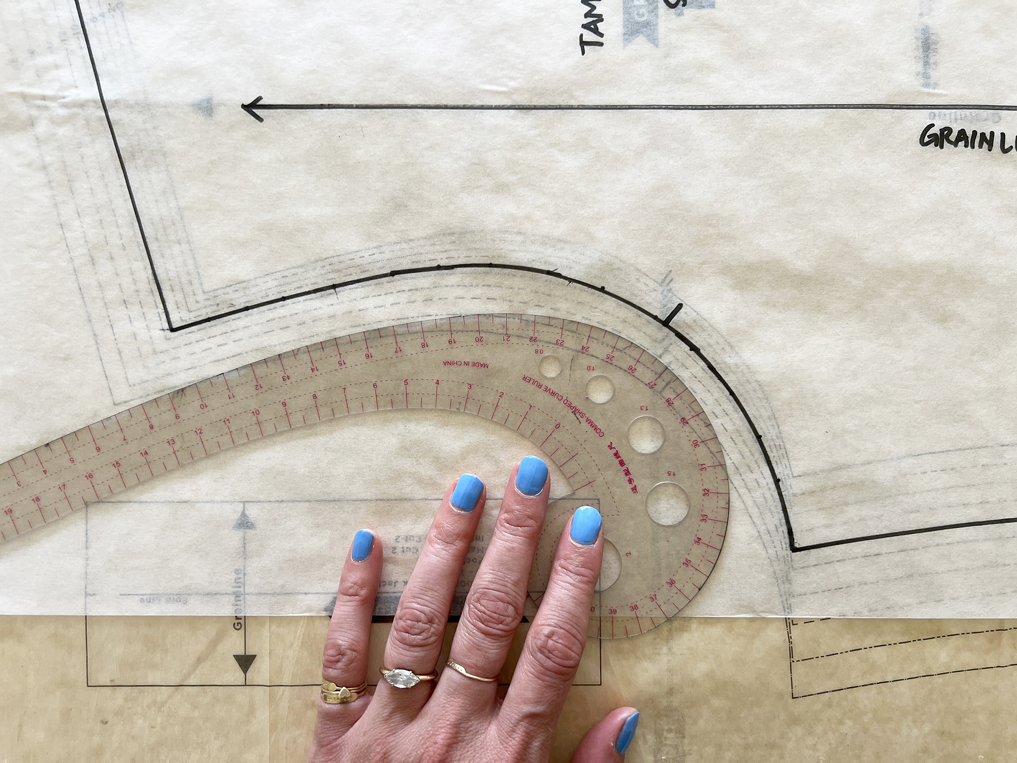 A curved ruler is used to trace the armscye on a sewing pattern.