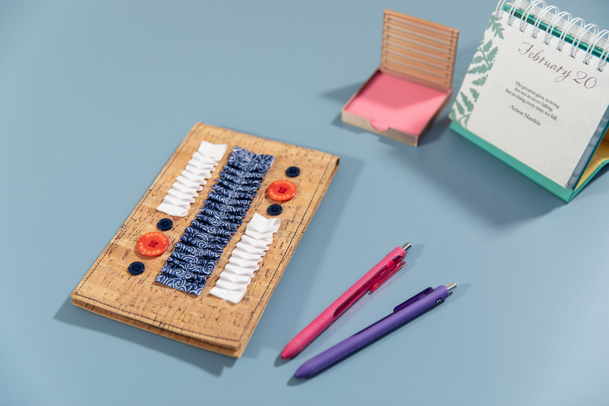 Cork notebook on a blue counter with office supplies arranged around it