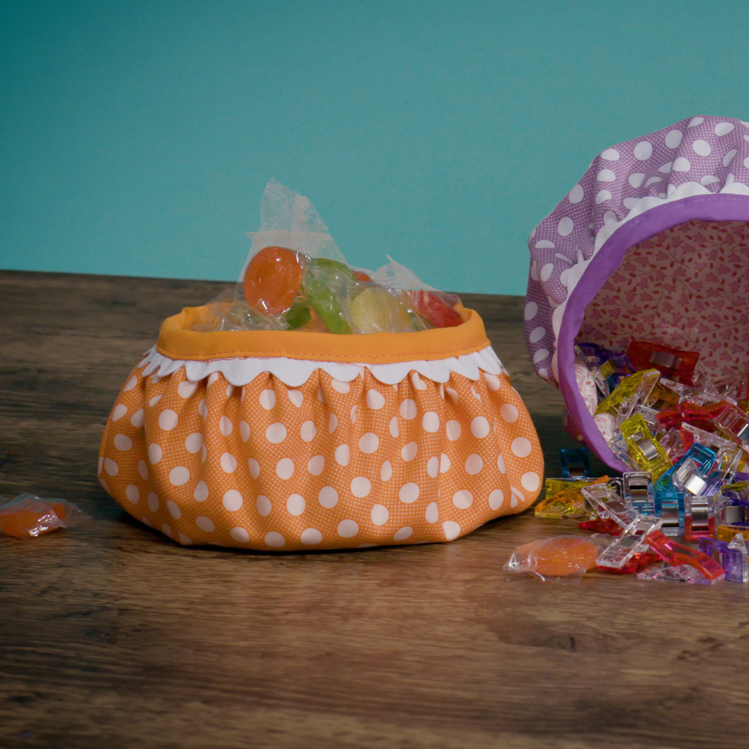 orange polka dot fabric bowl, filled with candy, on a wooden table