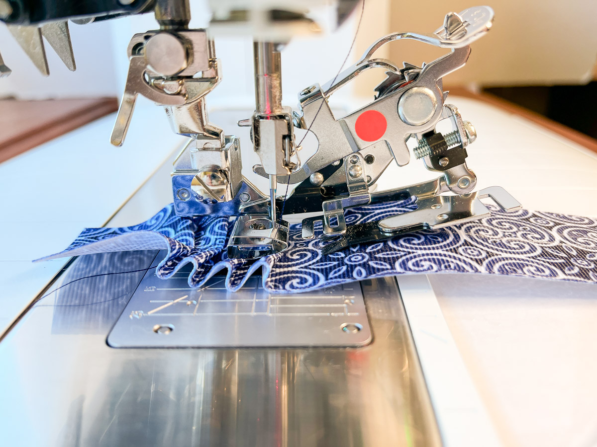 Side view of the blue fabric being fed through the machine, with pleats at the beginning