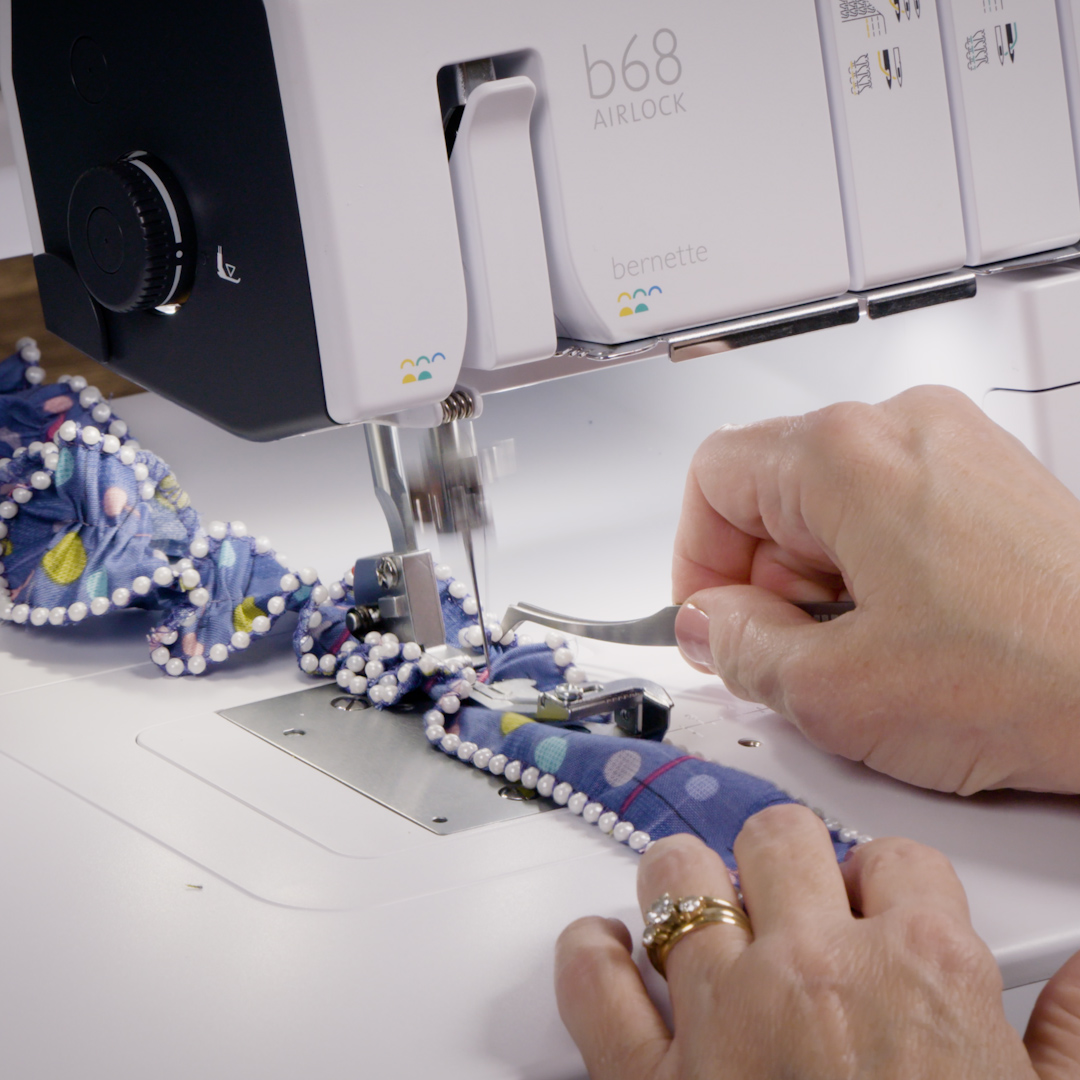 A hand with tweezers gathering the beaded fabric in the machine