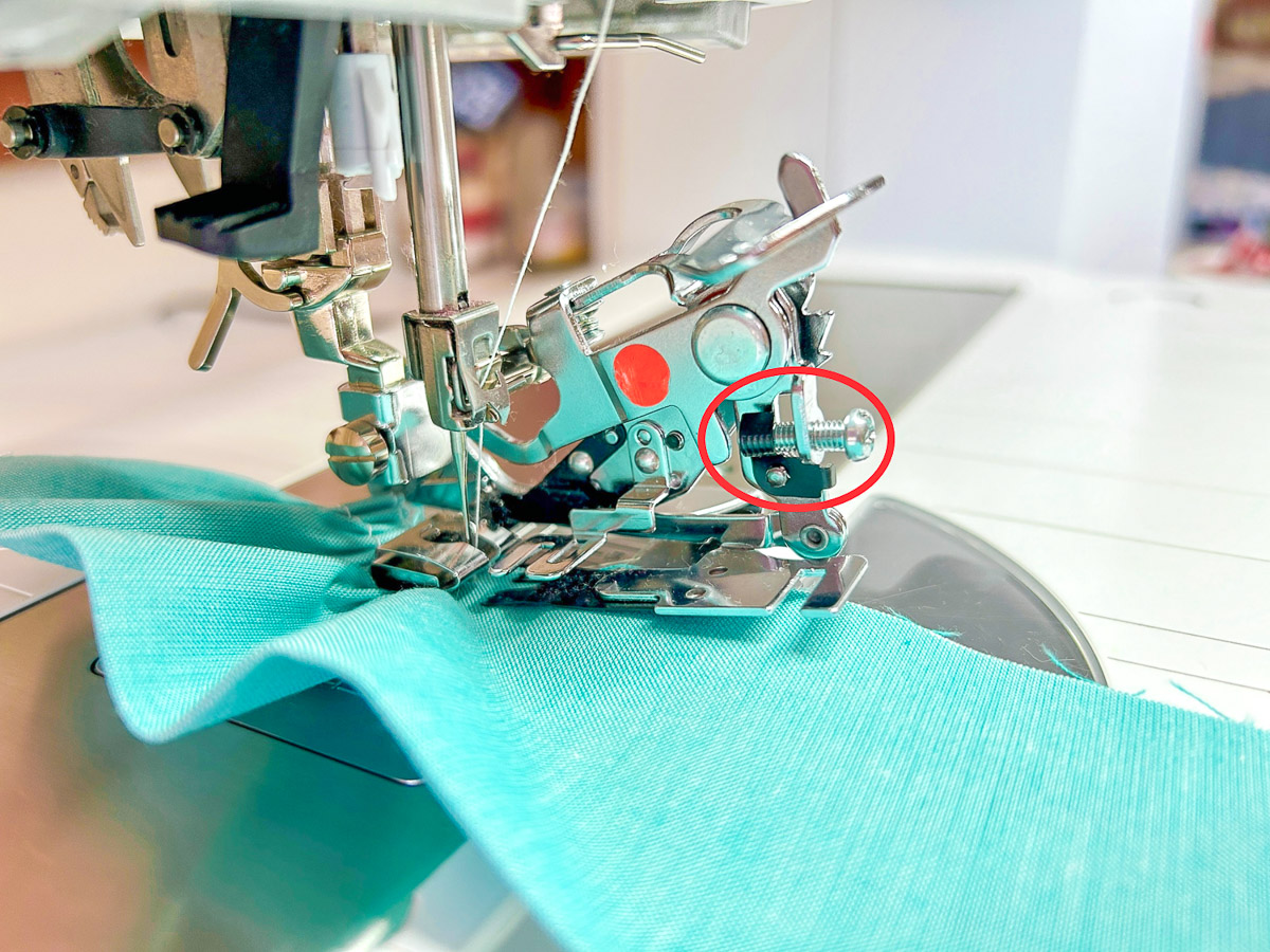 Red circle identifying adjusting screw location on machine with blue fabric
