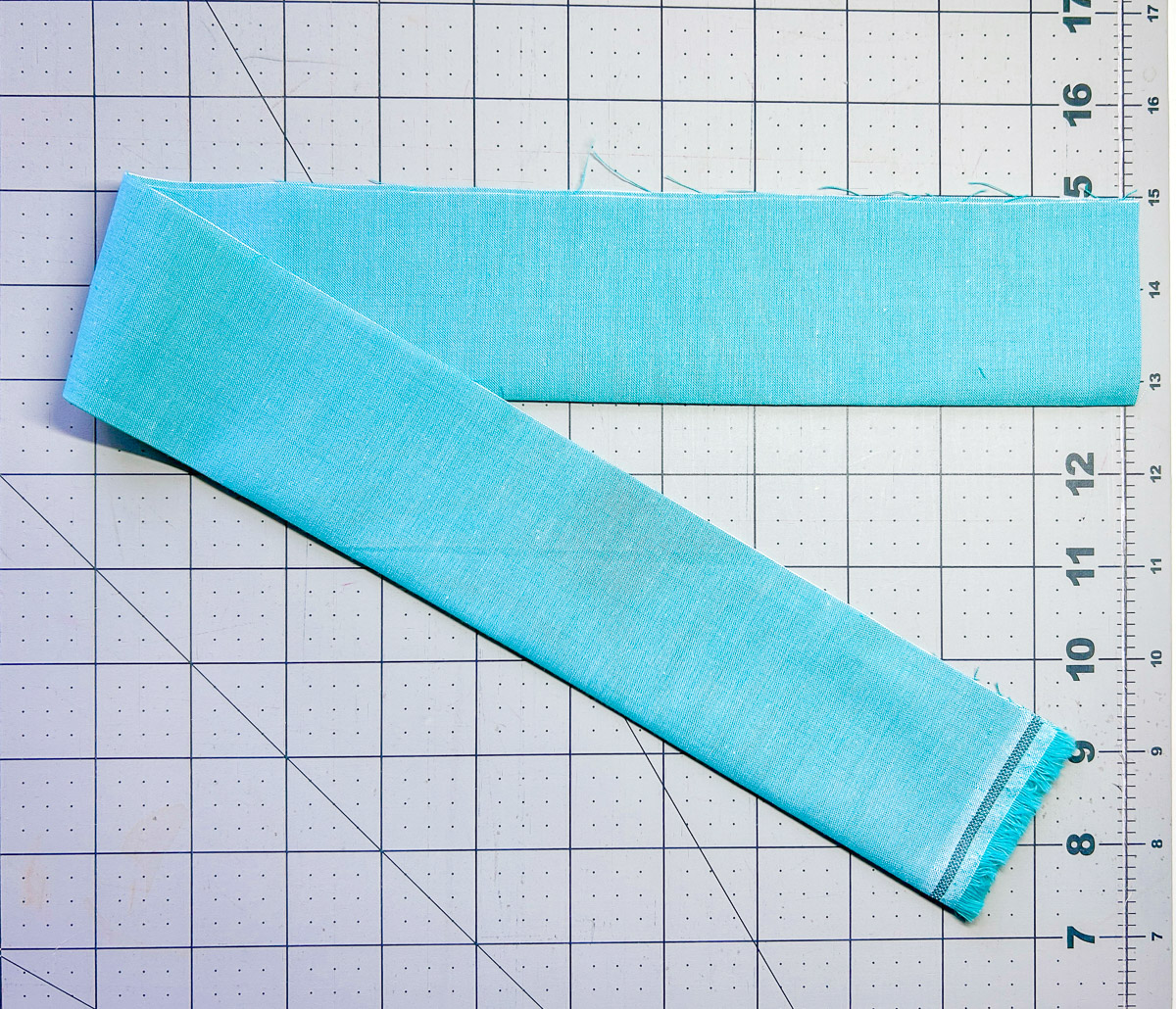 Blue fabric strip pressed in half against white cutting mat