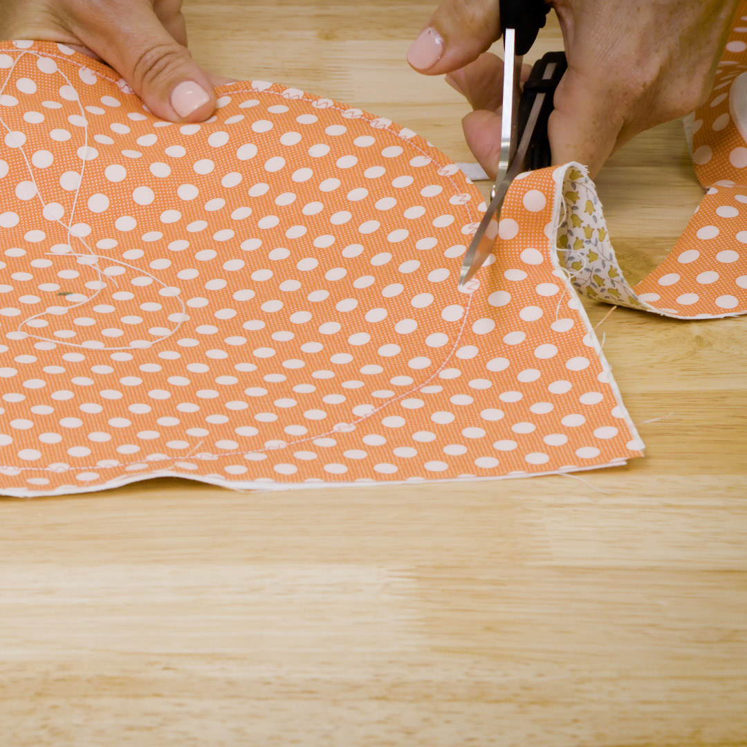 : side view of a left-handed sewer using sheers to cut a circle out of orange fabric
