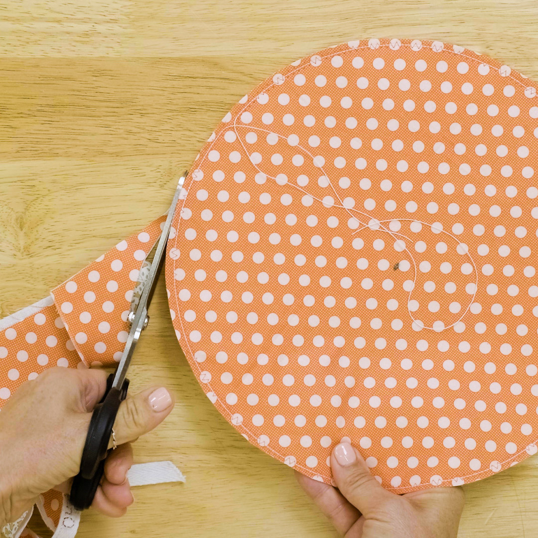 top view of a left-handed sewer using sheers to cut a circle out of orange fabric