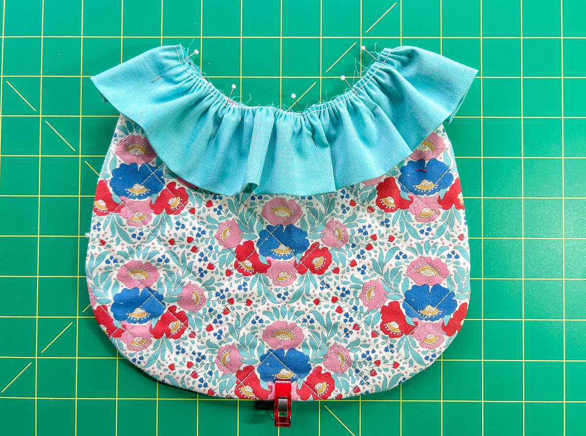 Blue ruffle pinned to colorful bib against green cutting mat