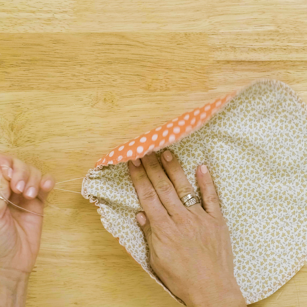 a hand is pulling two cords to cinch and gather a fabric circle