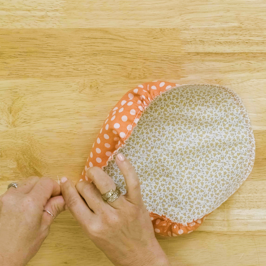 a hand is pulling two cords to cinch and gather a fabric circle