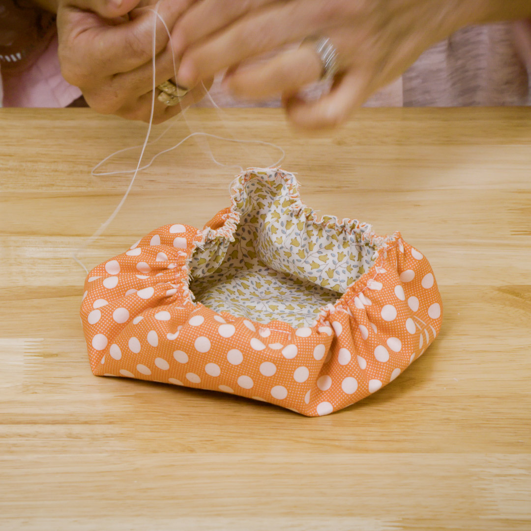 hands over the cinched orange fabric bowl, tying the cords into a knot