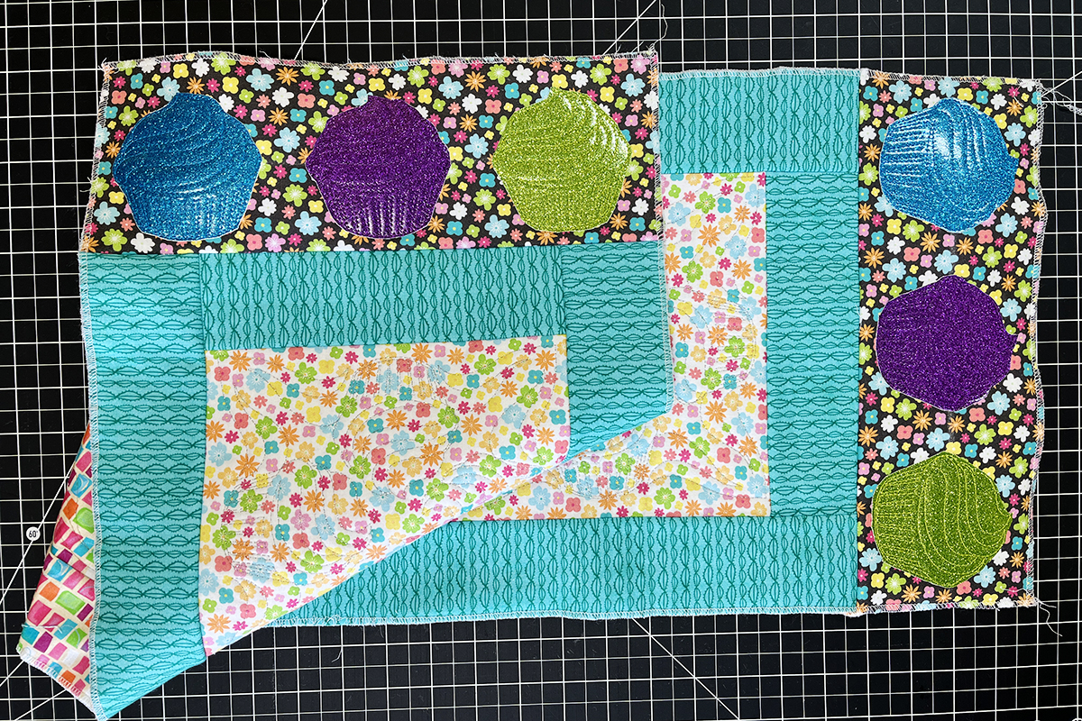 overhead view of three different cupcake-embroidered vinyl applique on multi-color fabric