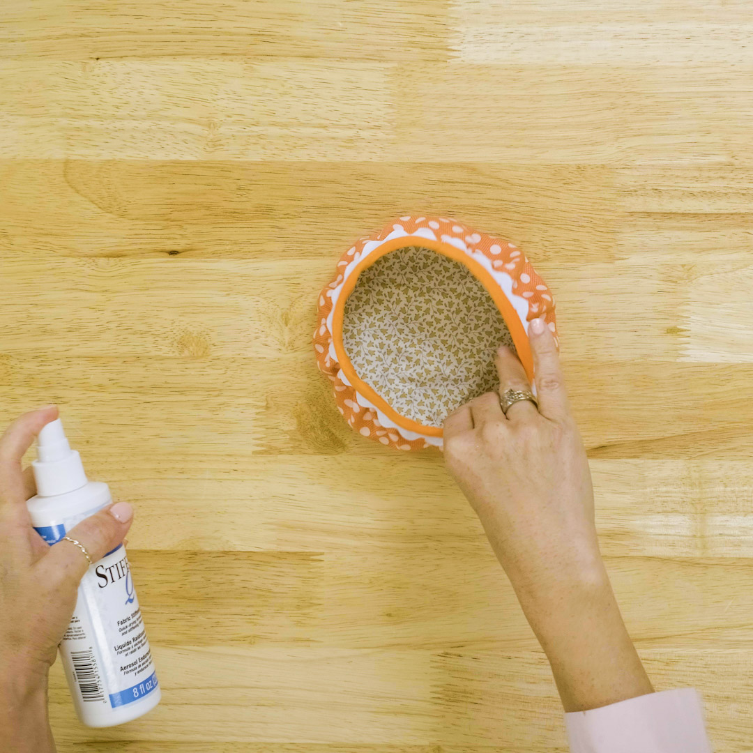 using a bottle of stiffener spray to moisten the finished orange fabric bowl