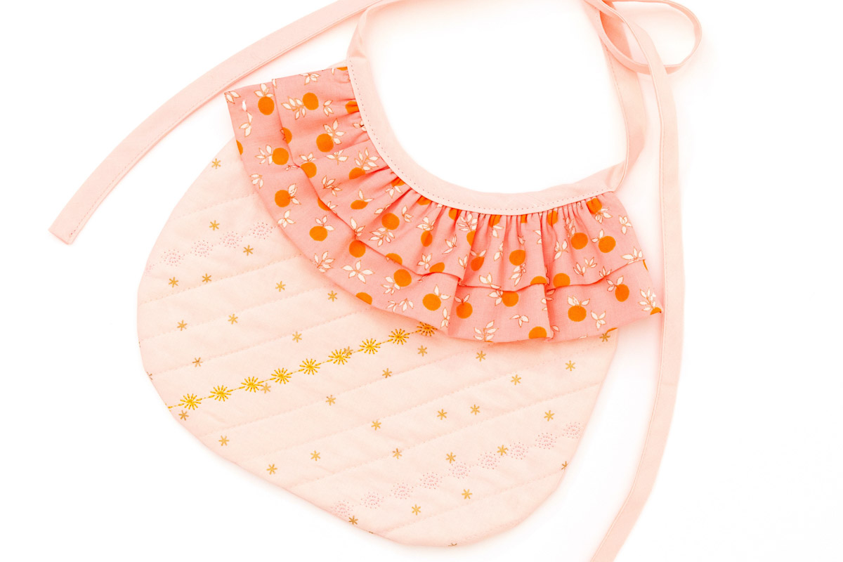 Peach colored bib with double ruffles against white background