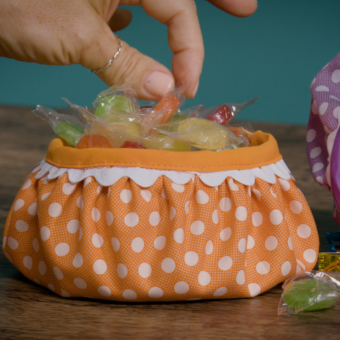 orange polka dot fabric bowl, filled with candy, on a wooden table