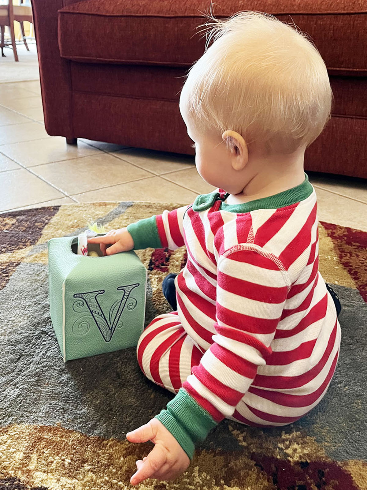 Baby with mint green tissue box embroidered "V" in room