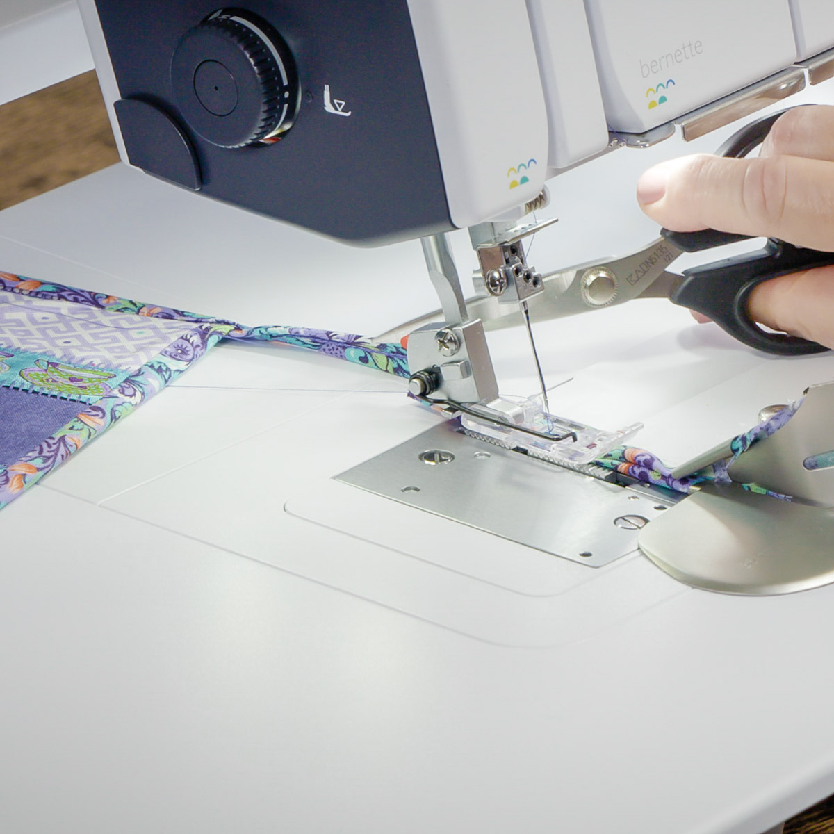 Scissors cutting the binding behind the serger foot.