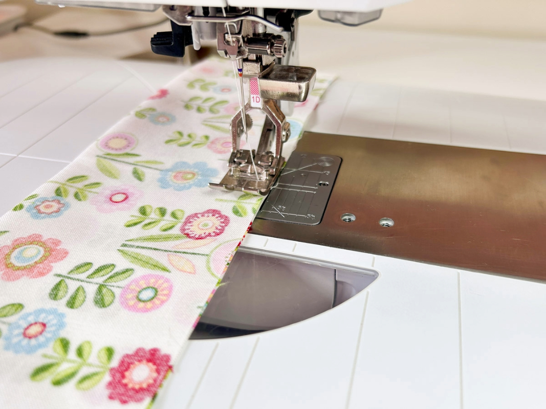 Close up view of the presser foot sewing stitches along the edge of the flowered fabric.