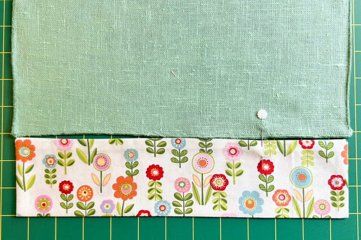 Overhead view of the sewn strip of flowered fabric being pinned to the plain green napkin.
