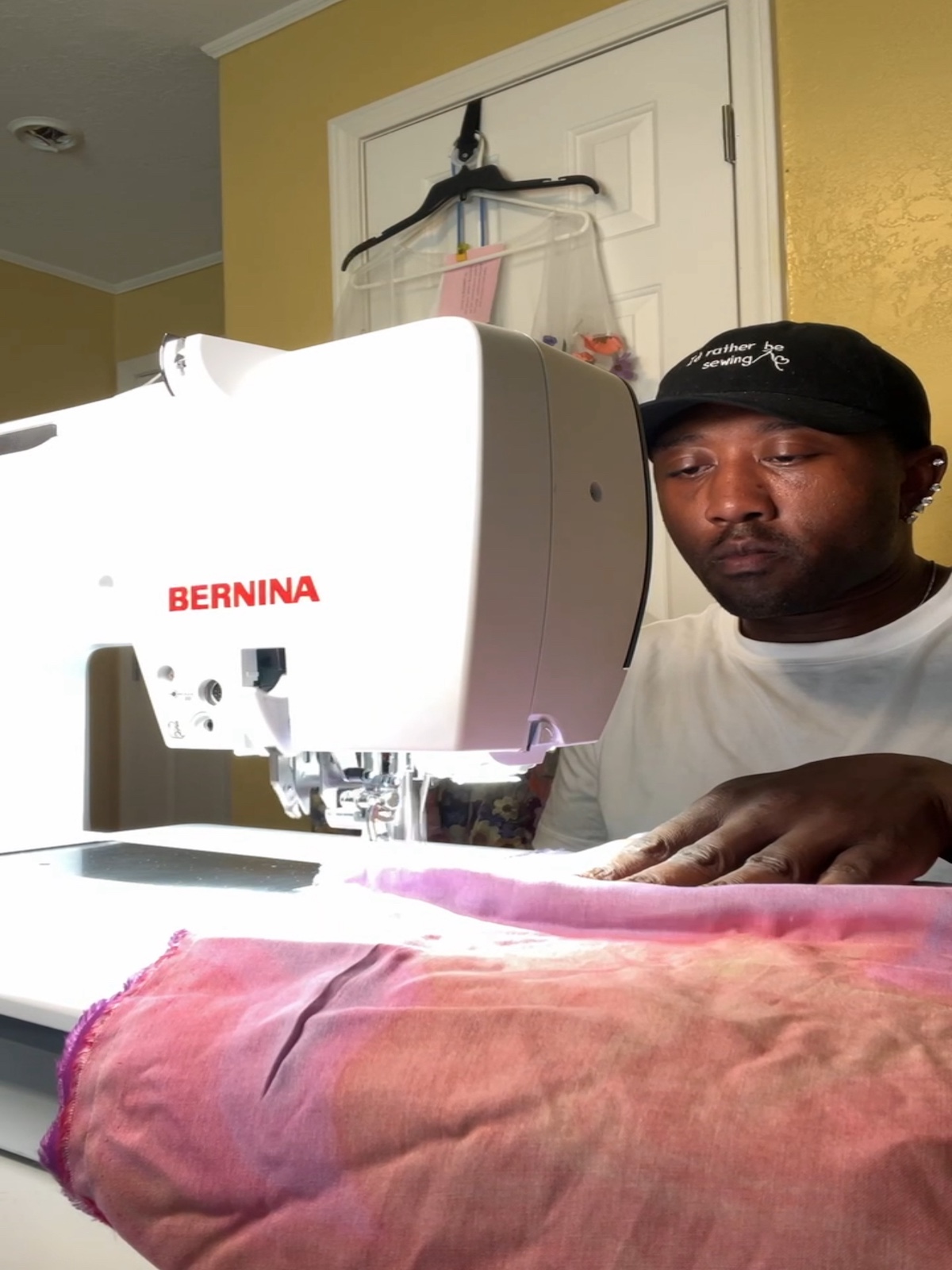 Black man wearing a hat sitting behind a sewing machine BERNINA B 790 PRO