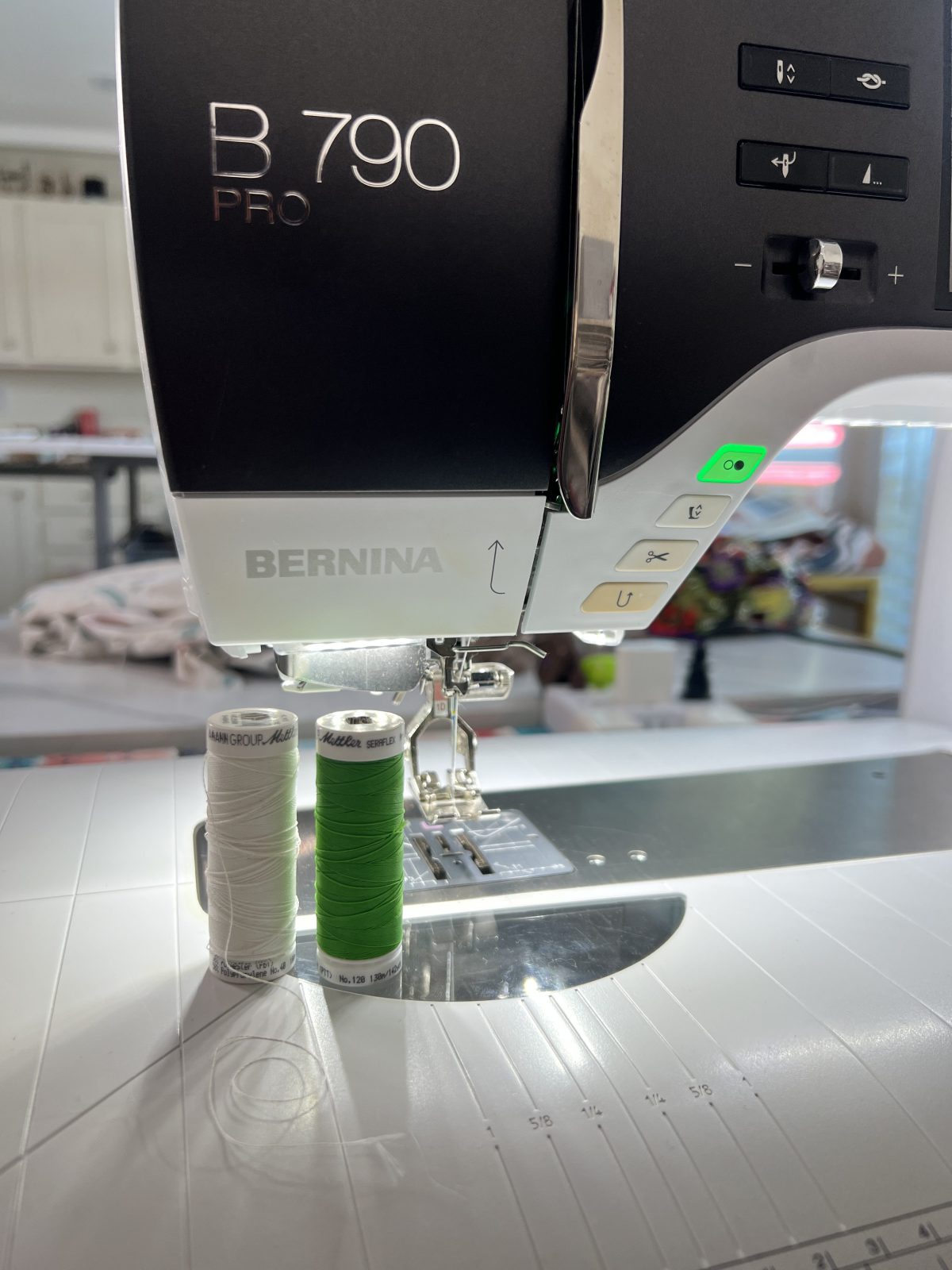 Close-up of a Bernina B 790 Pro sewing machine with two spools of Mettler thread, one white and one green, placed upright on the sewing surface beneath the presser foot.