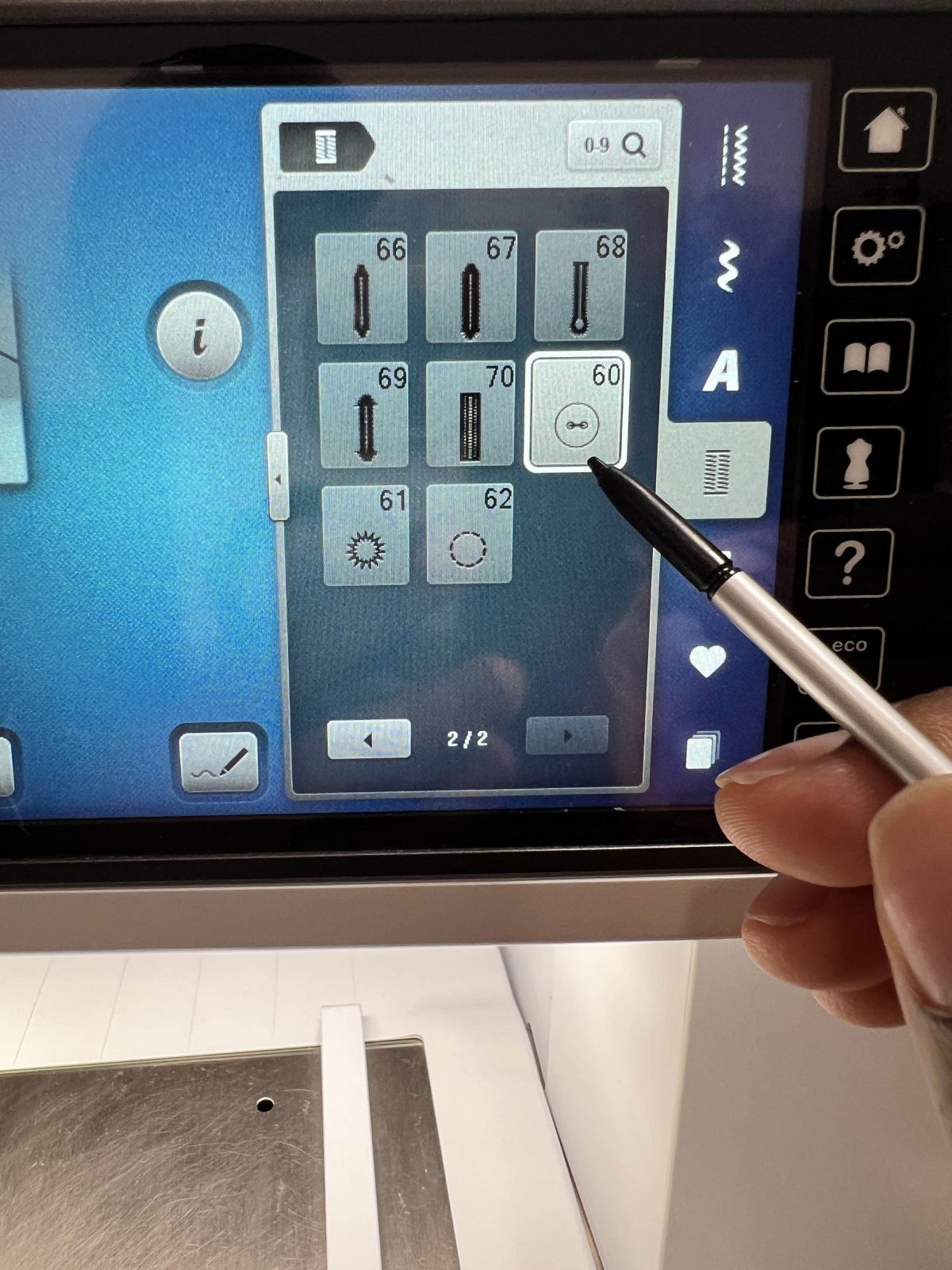 Close-up of the BERNINA B 790 PRO touchscreen showing different buttonhole stitch options. A hand is holding a stylus and tapping the buttonhole style labeled “60” on the screen. The metal stitch plate of the machine is visible below.
