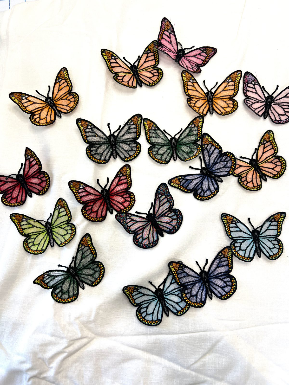 Colorful freestanding embroidered butterflies in pink, orange, blue, green, purple, and red arranged on white fabric.