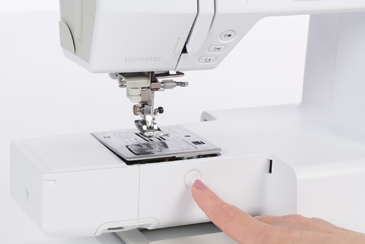 A finger pressing a button to release the stitch plate on a sewing machine